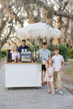 Family posing behind a mobile coffee bar in an outdoor setting with trees and large hanging moss