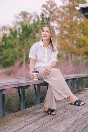Woman sitting on a bench holding a coffee cup in a natural outdoor setting