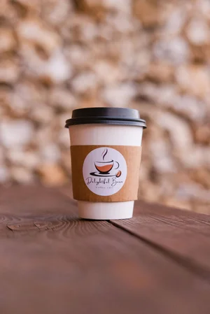 Coffee cup with Delightful Bean logo on table, blurred background.