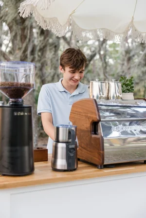 Young barista at outdoor coffee stand with espresso machine and grinder.